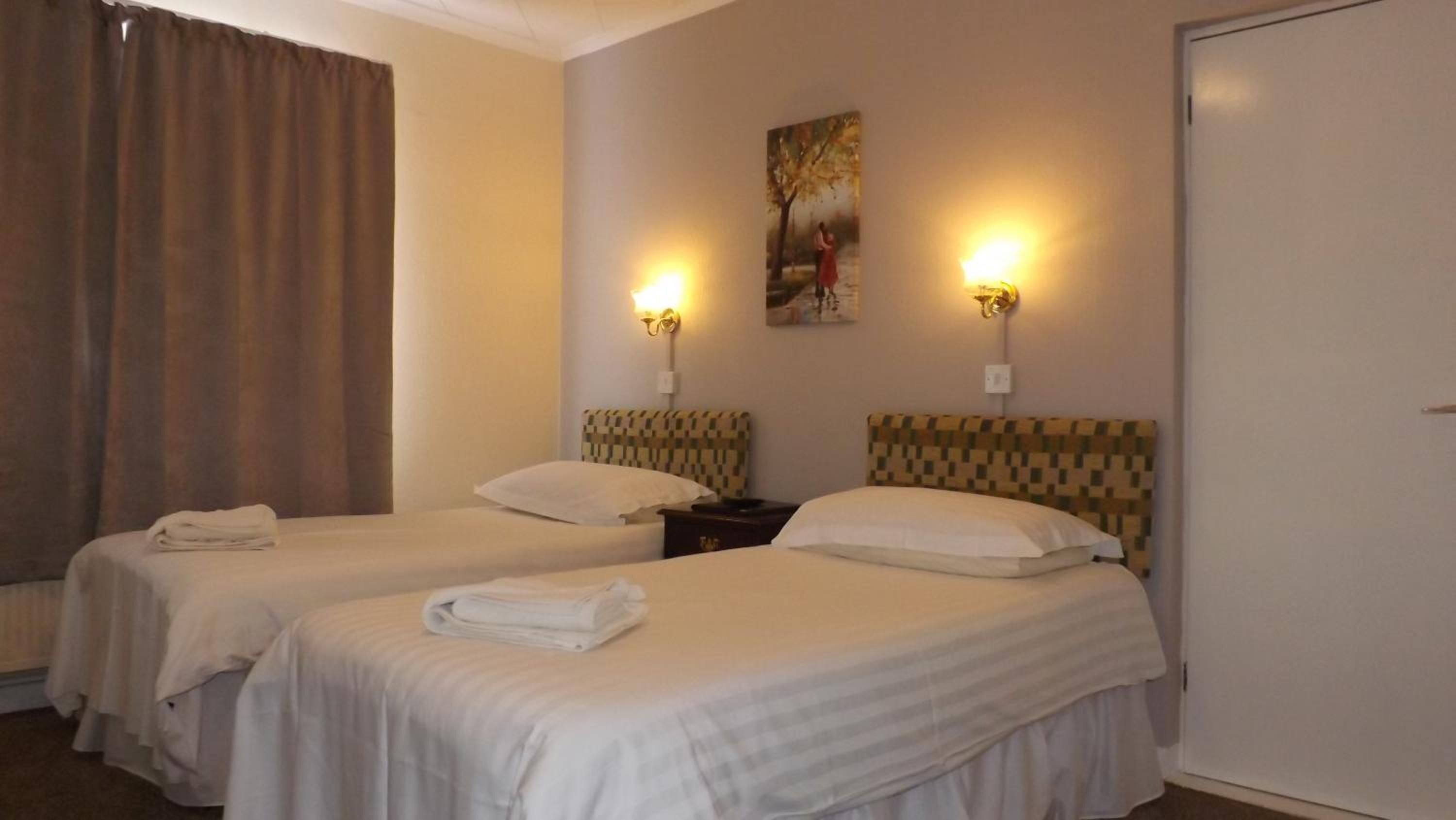 Une chambre d’hôtel avec deux lits, chacun doté d’une tête de lit et d’un oreiller. Deux lampes murales sont fixées de part et d’autre d’un tableau.