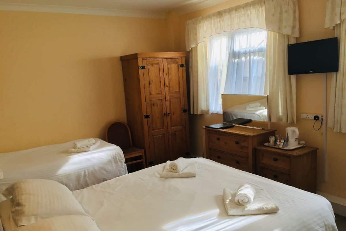A hotel room with two beds, a wooden wardrobe, a desk with a chair, a television, and a window with curtains.