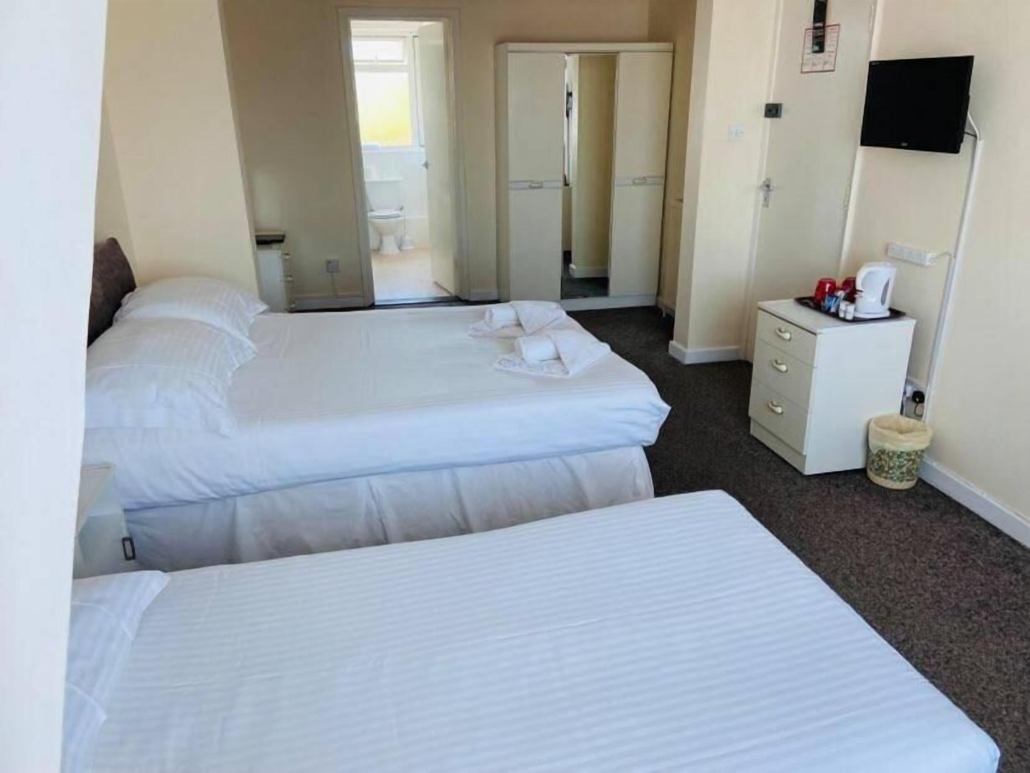 A hotel room with two beds, a small bedside table with a lamp, a TV mounted on the wall, and a bathroom visible through an open door.
