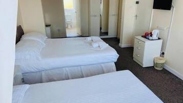 A hotel room with two beds, a small bedside table with a lamp, a TV mounted on the wall, and a bathroom visible through an open door.