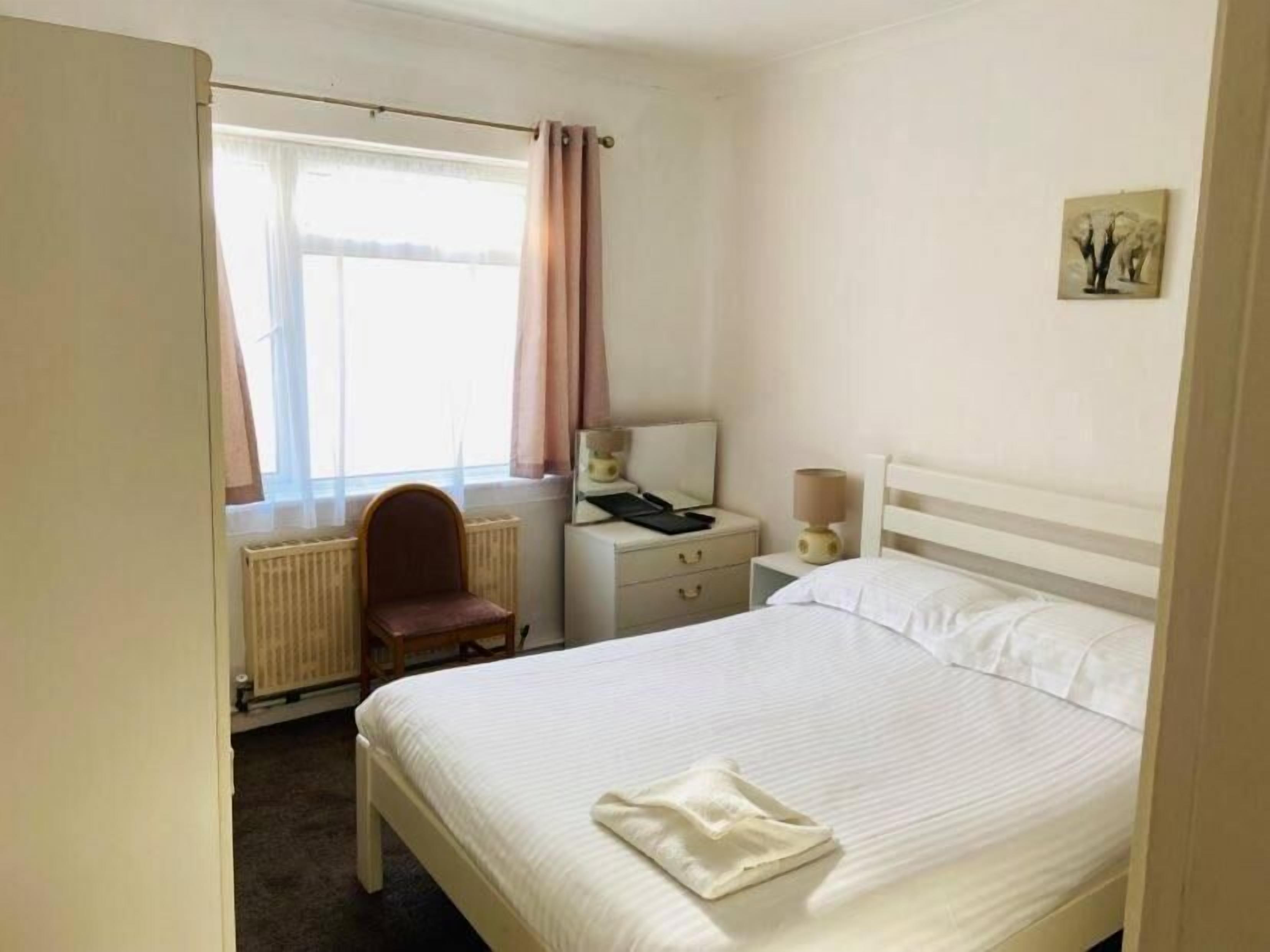 A hotel room with a bed, a chair, a nightstand, a lamp, a radiator, and a window with curtains.