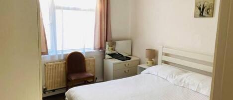 A hotel room with a bed, a chair, a nightstand, a lamp, a radiator, and a window with curtains.