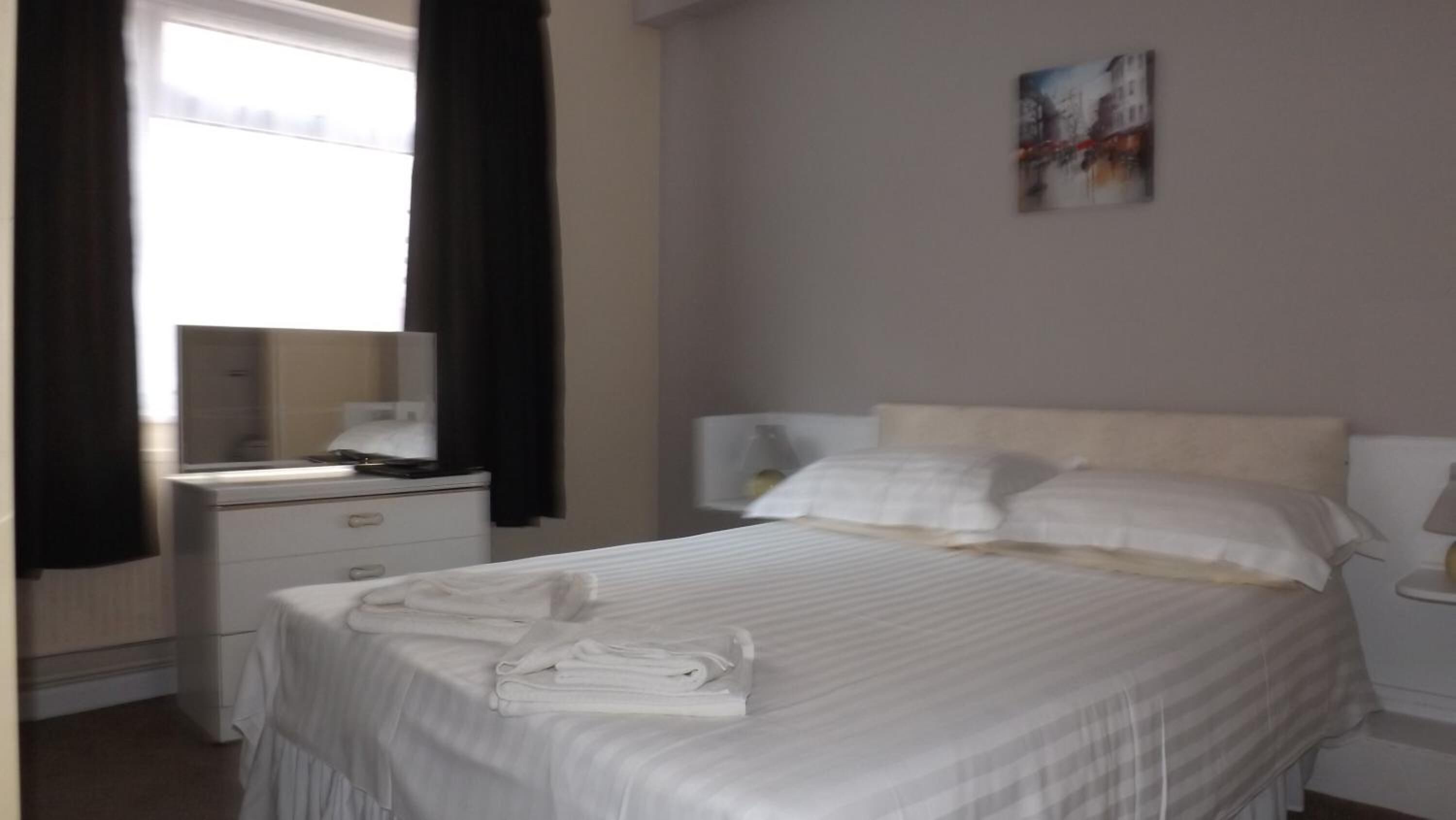A neatly made bed with white linens, a bedside table with a lamp, and a painting on the wall.