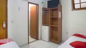 Habitación de hotel con cama, armario, refrigerador pequeño y televisor sobre una repisa.