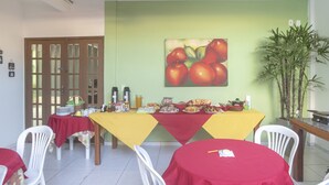 Un comedor con mesas cubiertas de manteles rojos, un cuadro de manzanas en la pared y una planta en maceta.