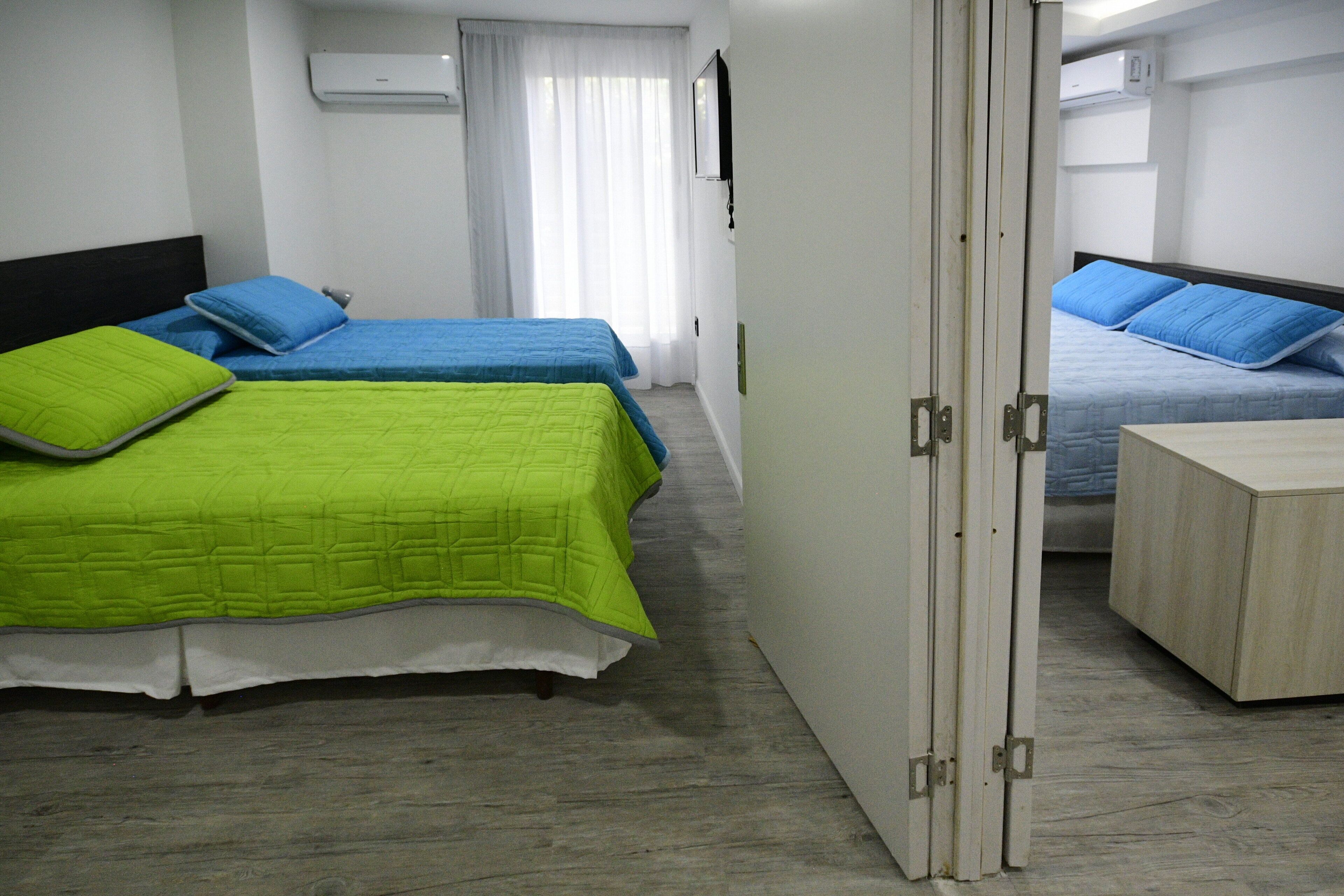 Habitación de hotel con dos camas, cada una con un edredón de diferente color, un armario de madera y una puerta corredera.