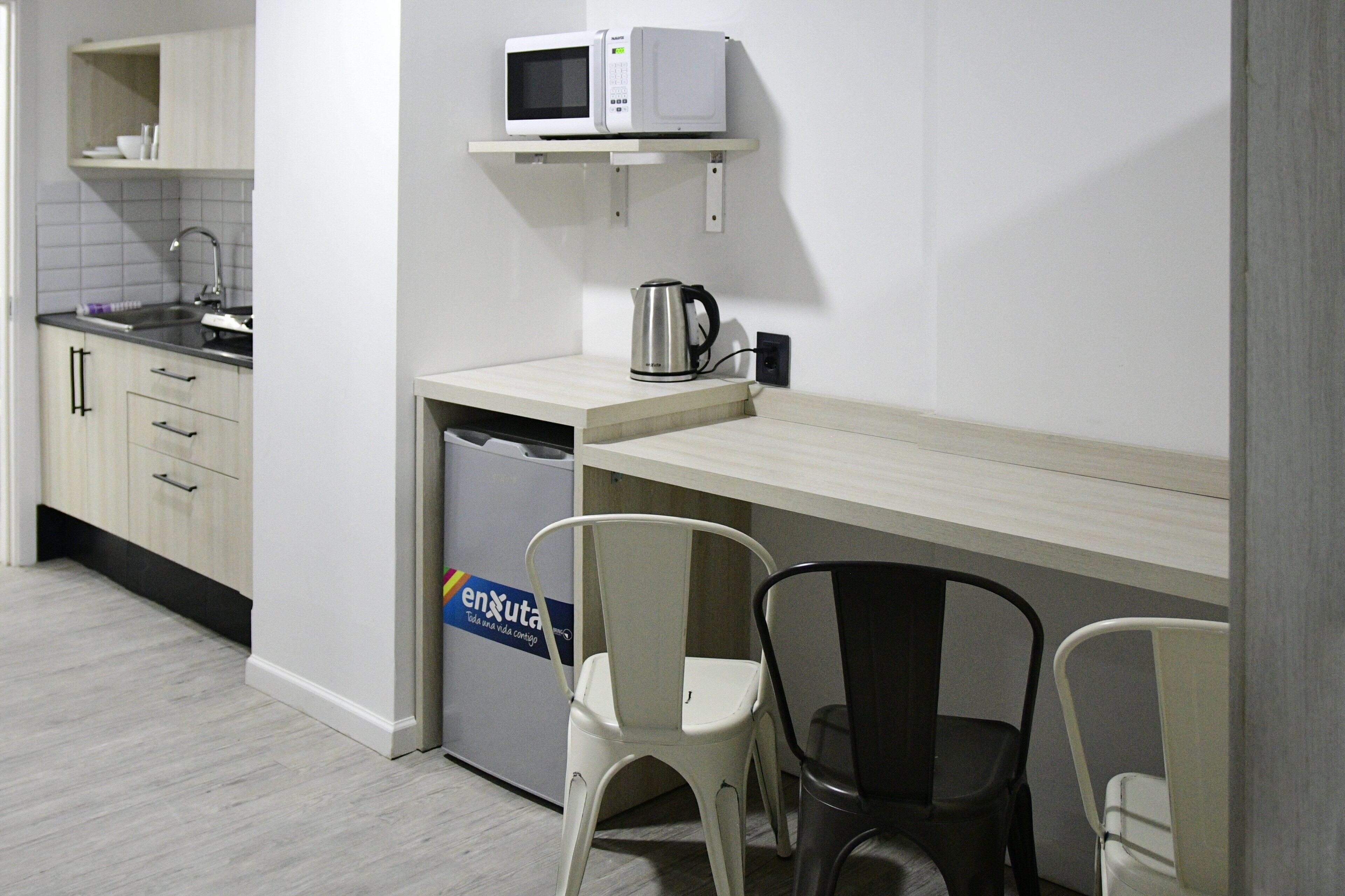 A compact kitchen with a microwave, kettle, and a dishwasher. There are two chairs and a small table.