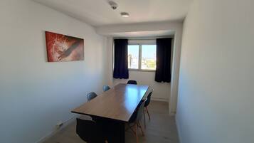 A conference room with a long table, four chairs, a ceiling-mounted security camera, and a window with curtains.