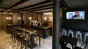 Zona de bar con una barra alargada, taburetes y una pantalla de televisión que muestra a una persona.