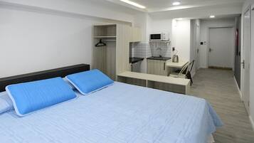 A bedroom with a bed, a desk, and a kitchenette.