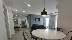 Un comedor moderno con una mesa redonda y sillas, una cocina al fondo, y un televisor de pantalla plana montado en la pared.