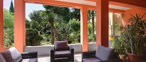 A covered outdoor seating area with wicker furniture and cushions, surrounded by orange walls and potted plants.