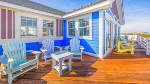A blue and white building with a wooden deck, outdoor seating, and a view of the ocean. - Premier Oceanfront Dog Friendly w/ Pool, Elevator, Hot Tub, Theater, Game Rooms (Salvo)
