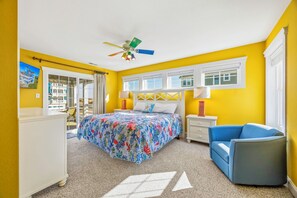 Een slaapkamer met een bed, een plafondventilator, een nachtkastje, een lamp, een stoel en een raam.