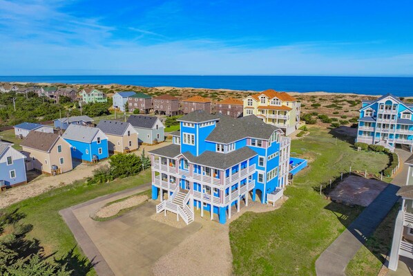 A coastal residential area with houses, a prominent blue building with multiple stories and balconies, and a clear view of the ocean.