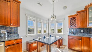 A kitchen with wooden cabinets, a granite countertop, a central island, and large windows. - Premier Oceanfront Dog Friendly w/ Pool, Elevator, Hot Tub, Theater, Game Rooms (Salvo)