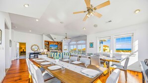 A spacious dining area with a long wooden table, multiple chairs, and a ceiling fan. - Premier Oceanfront Dog Friendly w/ Pool, Elevator, Hot Tub, Theater, Game Rooms (Salvo)