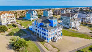 A coastal residential area with multiple two-story houses, some with balconies and a prominent blue house in the center. - Premier Oceanfront Dog Friendly w/ Pool, Elevator, Hot Tub, Theater, Game Rooms (Salvo)