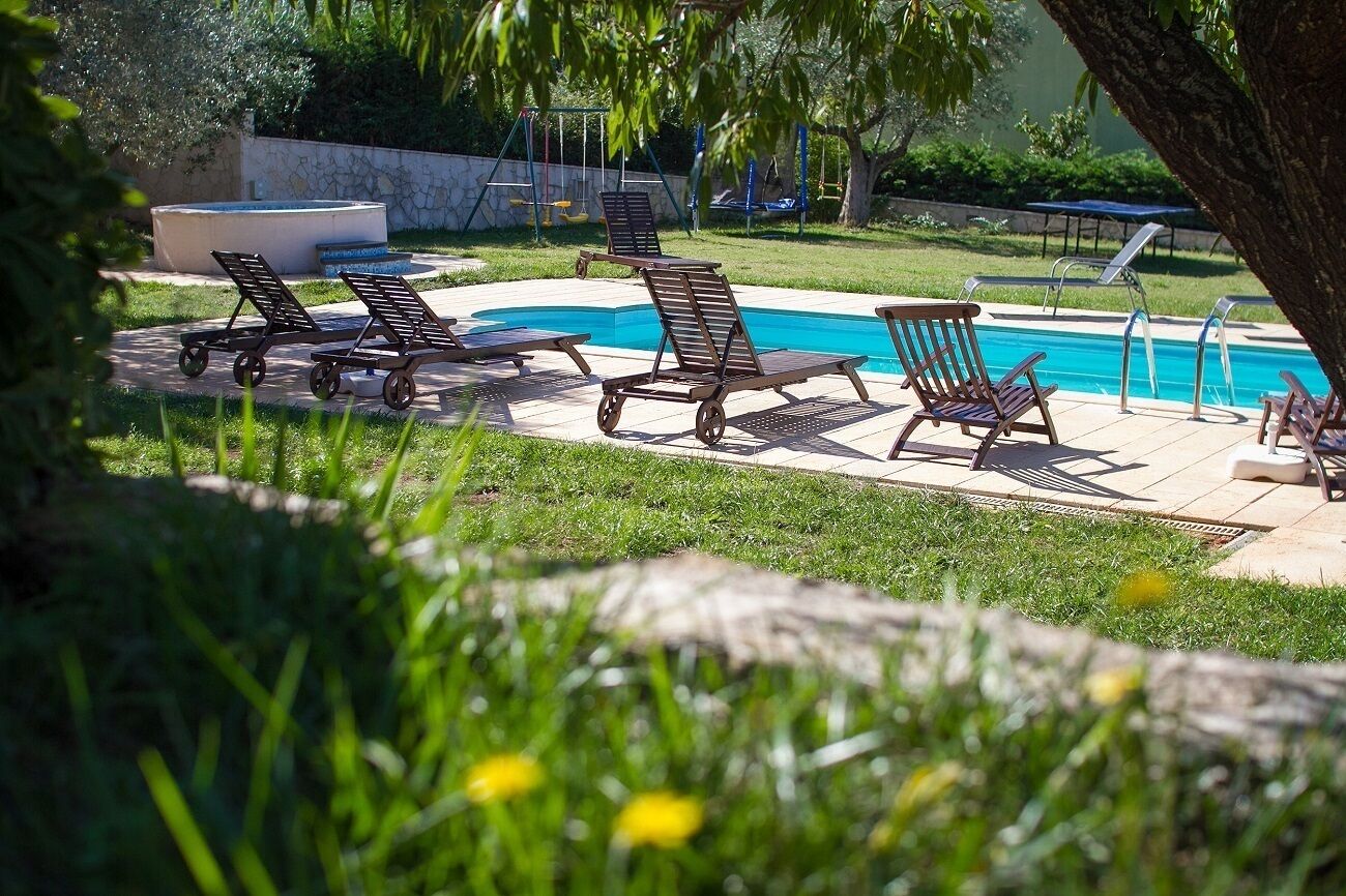 Un espace piscine avec des chaises longues et, au fond, une aire de jeux pour enfants.