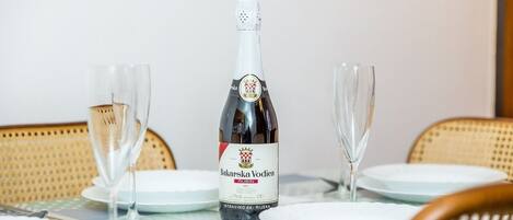 Uma garrafa de champanhe Bakarska Vodica RIBIN sobre uma mesa com dois copos vazios, rodeada por pratos brancos e talheres.