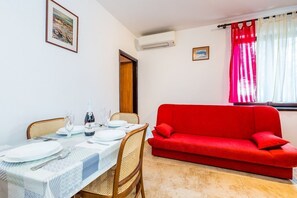 Un coin repas avec une table dressée pour deux personnes, un canapé rouge et une fenêtre avec des rideaux.