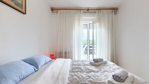 Un dormitorio con cama, cortinas blancas, una lámpara roja y vistas al exterior.