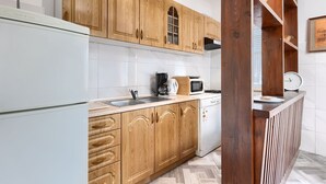 Una cocina con armarios de madera, un refrigerador blanco, cafetera, microondas y lavavajillas.