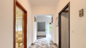 Un pasillo con suelo de baldosas, una puerta de madera a la derecha y un baño a la izquierda.