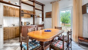 Comedor con mesa y sillas de madera, cocina con armarios de madera y vista a zonas verdes.