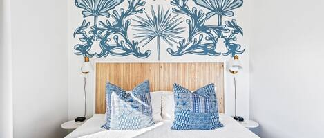Una cama bien hecha con un edredón estampado y almohadas, un cabecero de madera y dos lámparas de noche.