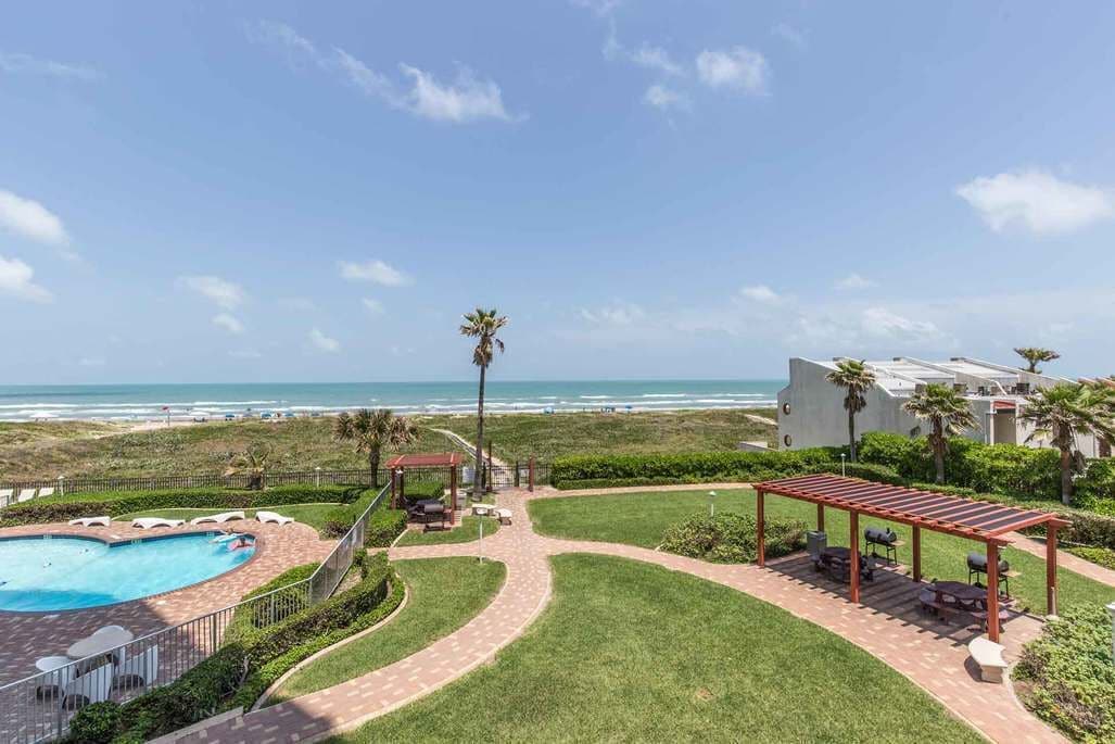 Ein Poolbereich mit Meerblick, eine überdachte Terrasse und ein angelegter Garten.