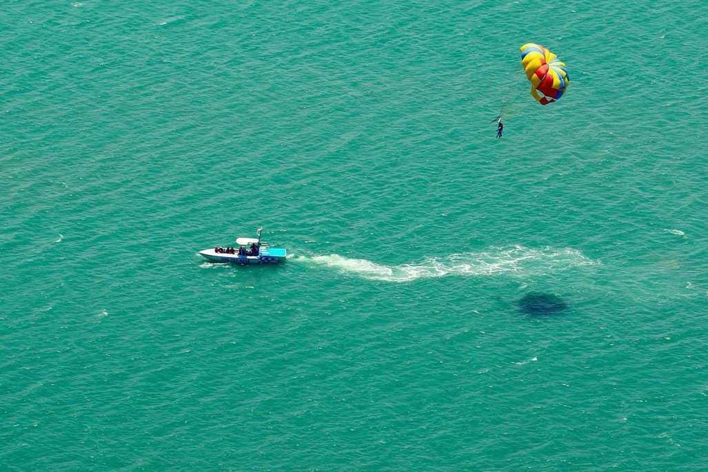 Ein Gleitschirmflieger über dem Meer mit einem Boot und einer Person im Wasser.