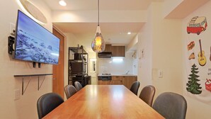 Una cocina moderna con una mesa y sillas de madera, un televisor montado en la pared y una isla de cocina con horno integrado.