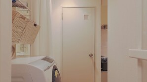 Un área de lavandería con lavadora, una puerta que da a una habitación y suelo de madera.