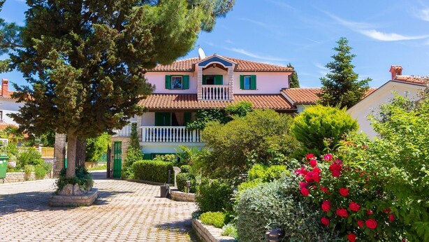 Ein zweistöckiges Haus mit einem Ziegeldach, einem Balkon mit weißen Geländern und einem Garten mit roten Blumen.
