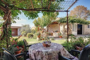 Relax in the serene patio surrounded by lush greenery and a charming stone building.