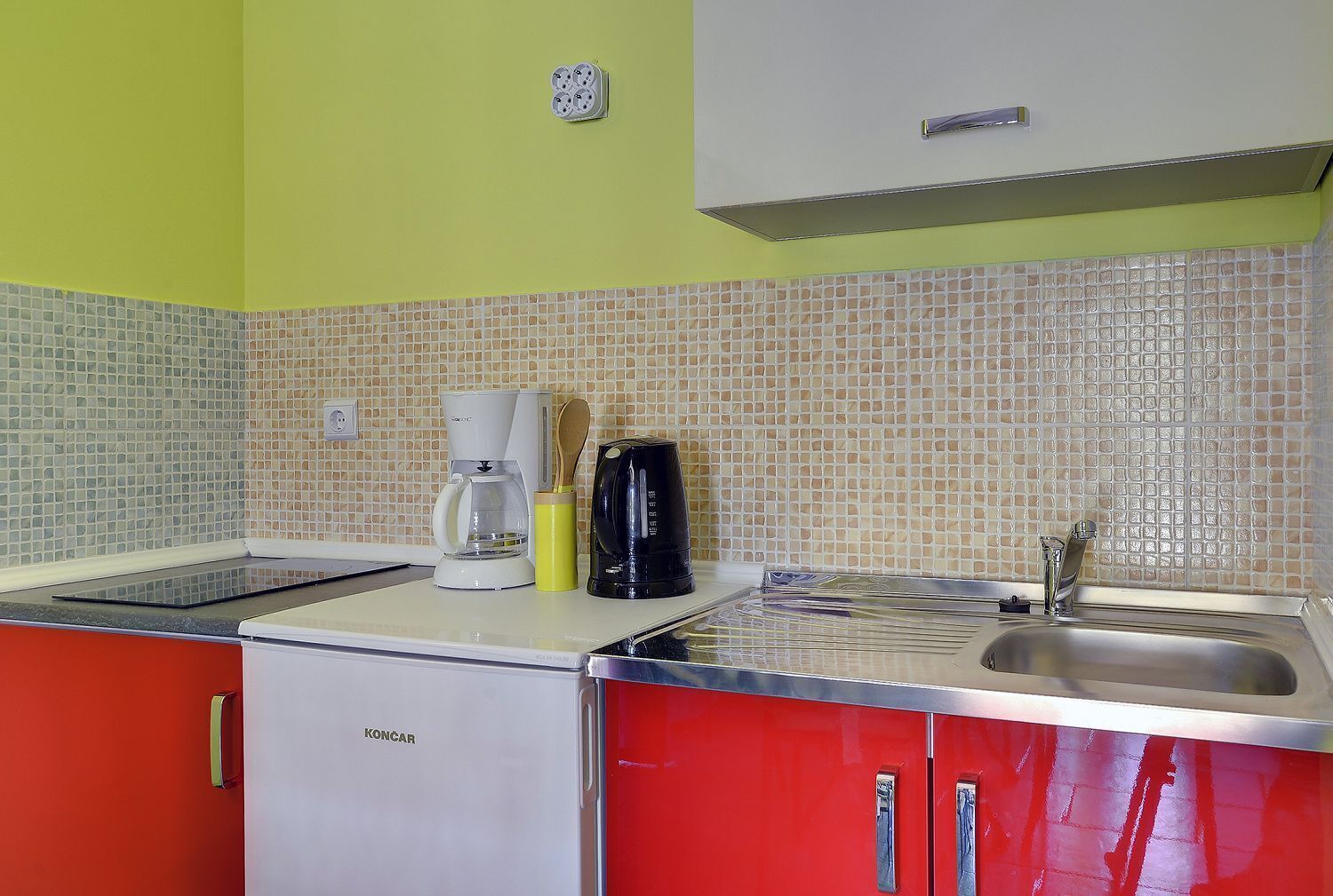A compact kitchen with a coffee maker, a kettle, and a toaster on the counter.