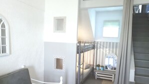 Quarto com uma cama de solteiro, uma mesa pequena e um banco.