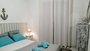 Quarto com cama, almofadas, mesa de cabeceira, luminária e um objeto decorativo na parede.