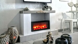 Uma sala de estar com lareira, televisão fixada na parede e um espaço de jantar com mesa e cadeiras.