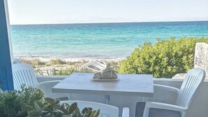 Um terraço com mesa e cadeiras, com vista para uma praia e água azul cristalina.