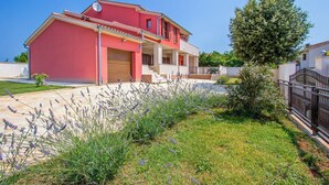 A two-story house with a red facade, a covered porch, and a small garden with lavender plants. - Apartment 500 meters to beach (Banjole)