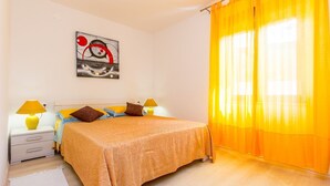 A bedroom with a bed, two bedside tables with lamps, a painting on the wall, and a window with yellow curtains. - Apartment 500 meters to beach (Banjole)