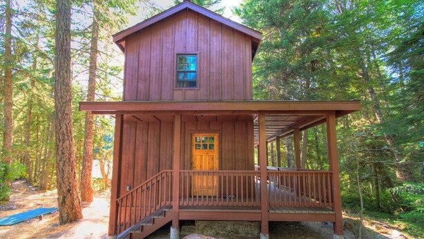 A wooden cabin with a porch and a door, surrounded by trees. - Doig Cabin: Support a great cause while on vacation! (Government Camp)