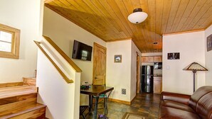 A wooden staircase leading to a dining area with a table and chairs, a kitchen with appliances, and a leather couch. - Doig Cabin: Support a great cause while on vacation! (Government Camp)