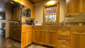 A kitchen with wooden cabinets, a stainless steel refrigerator, a window with blinds, and a tiled backsplash. - Doig Cabin: Support a great cause while on vacation! (Government Camp)
