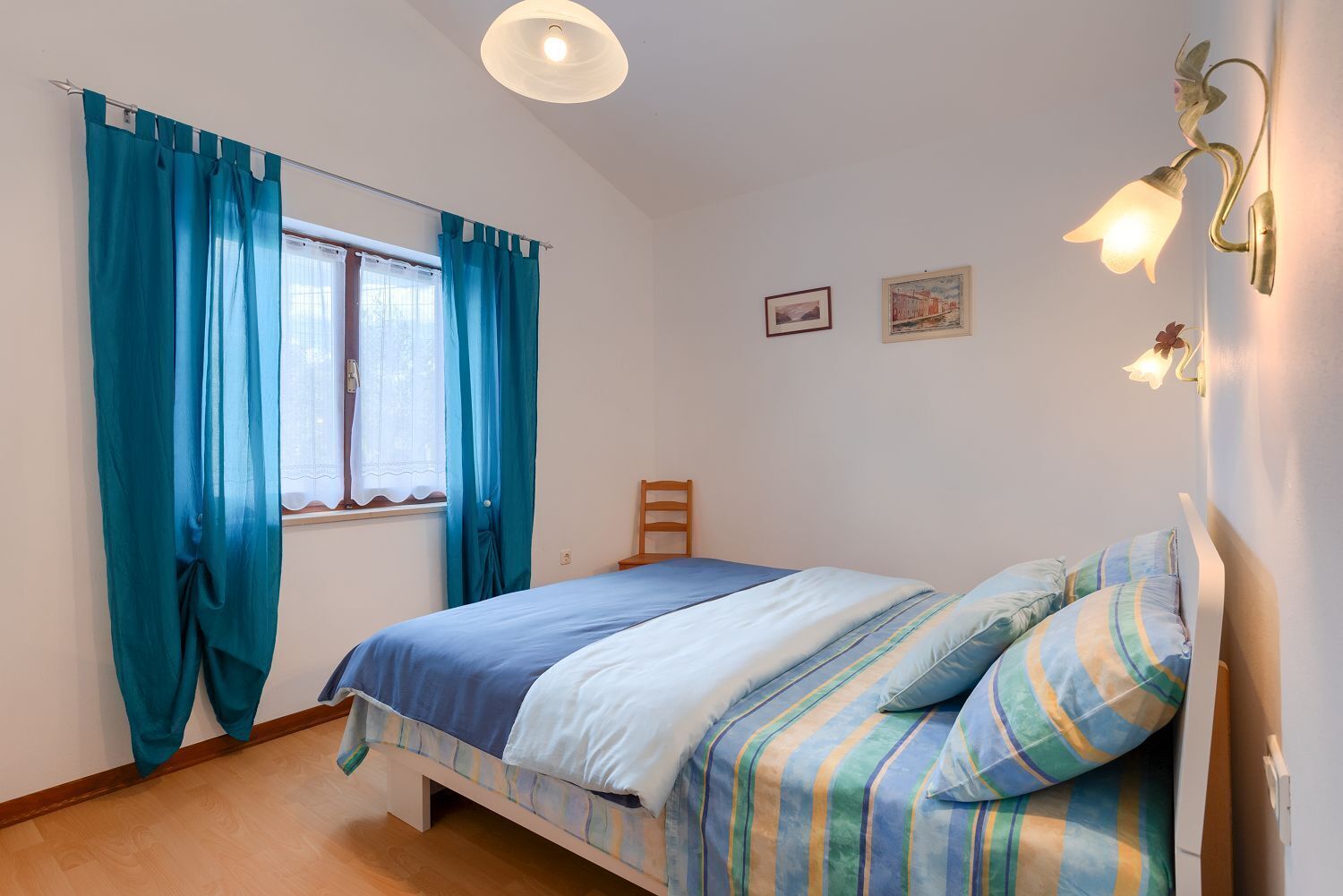 Een slaapkamer met een bed, gordijnen, een stoel en wandlampen.