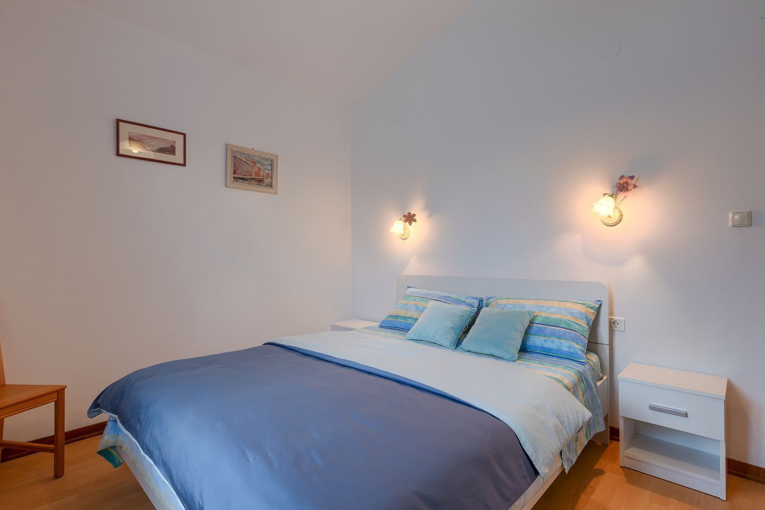 Un dormitorio con cama, mesitas de noche e iluminación en la pared.