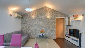Un salon moderne avec un mur d’accent en pierre, un canapé gris, une table basse en verre et un téléviseur à écran plat.