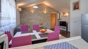 Un coin repas avec un mur en pierre, une table entourée de chaises, un saladier rempli de fruits et un téléviseur en arrière-plan.